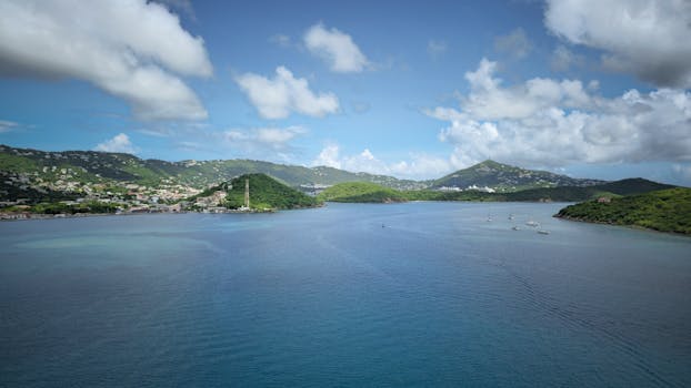 Tarif Breathtaking view of the Caribbean Sea with green hills and boats under a blue sky.